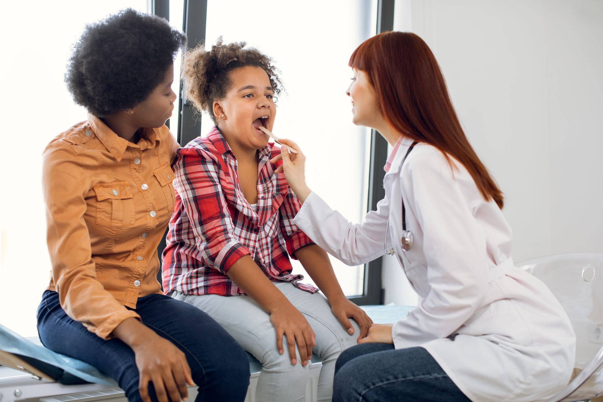 Doctor examining a smiling child while a caregiver sits nearby in a clinic