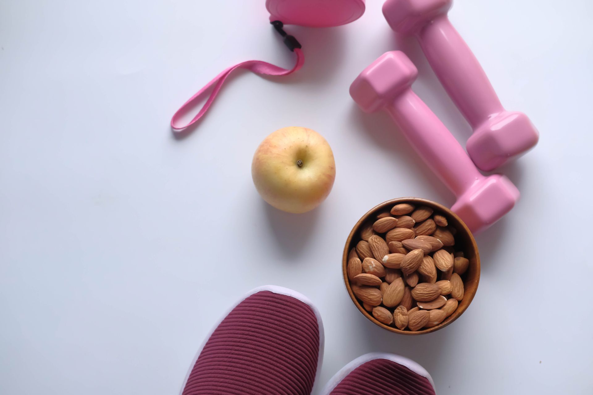 Pink workout gear with dumbbells, apple, and a bowl of almonds on a light surface