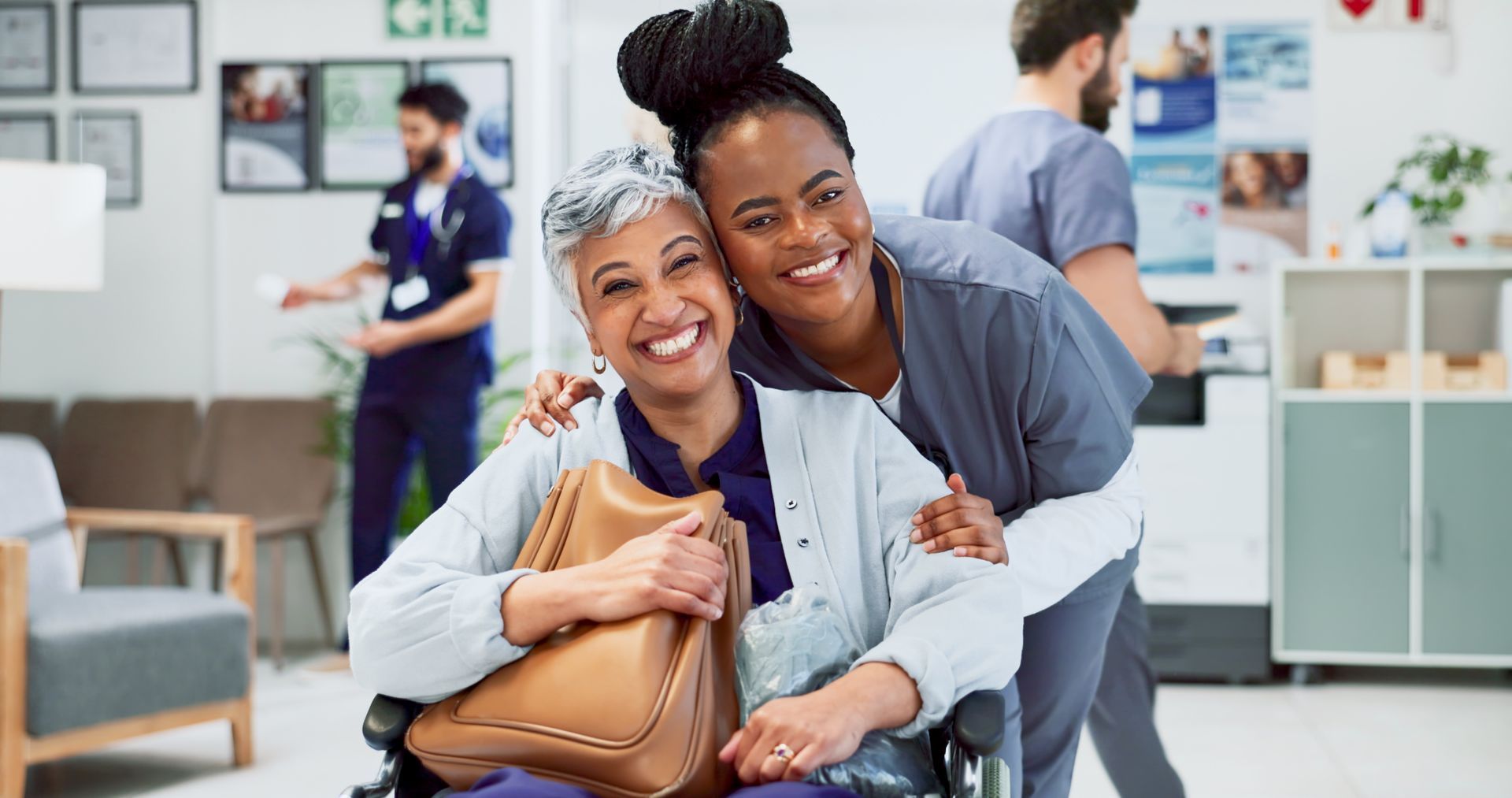 Smiling caregiver hugs an elderly woman in a clinic waiting area, with staff and patients in the background