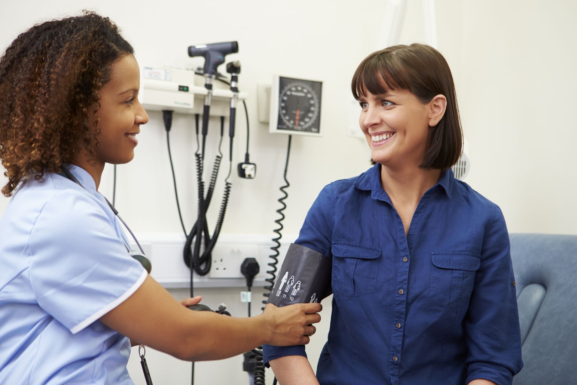 Doctor taking a patient's blood pressure in a clinic, both smiling.