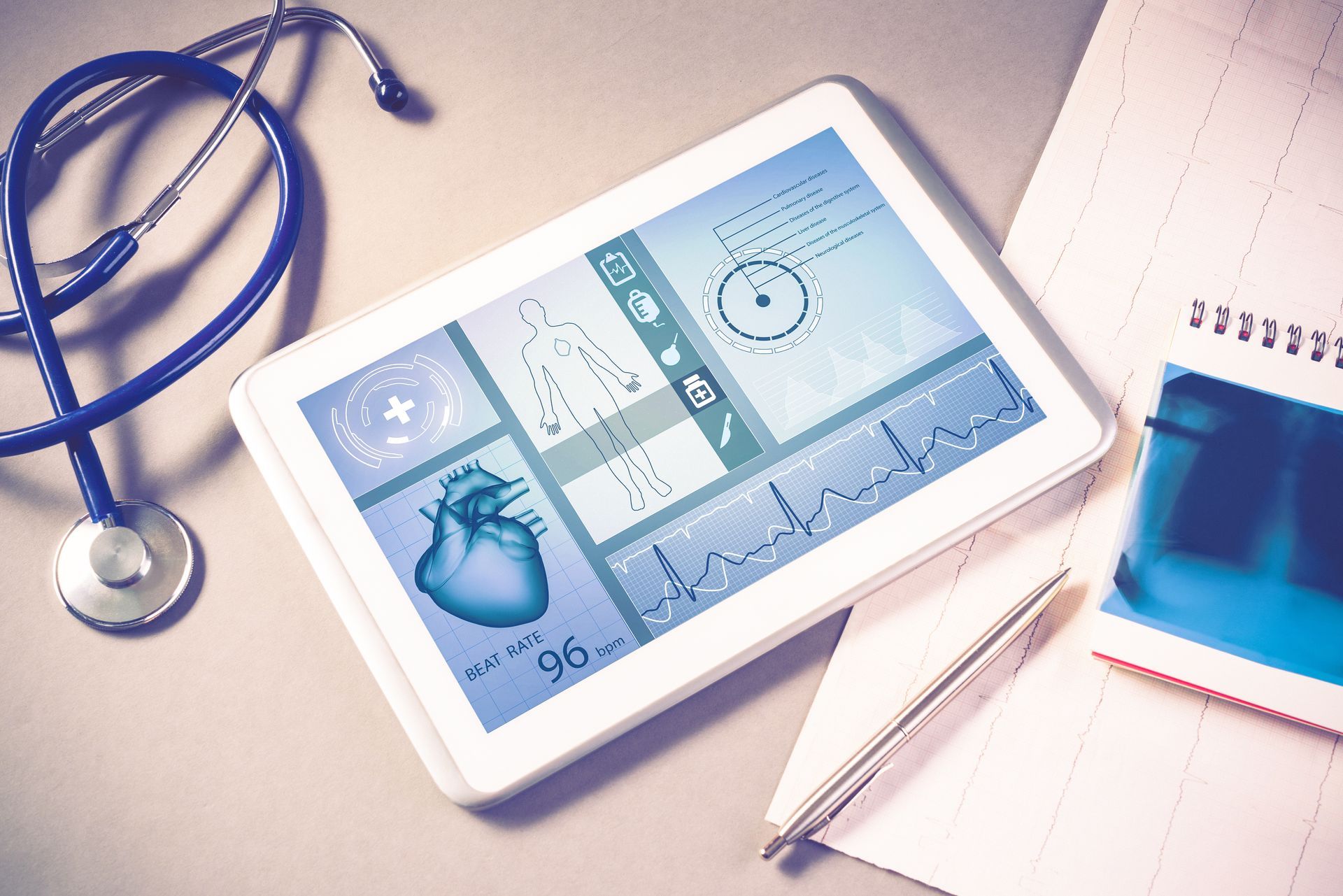 Tablet with medical dashboard on a desk beside a stethoscope and notebook