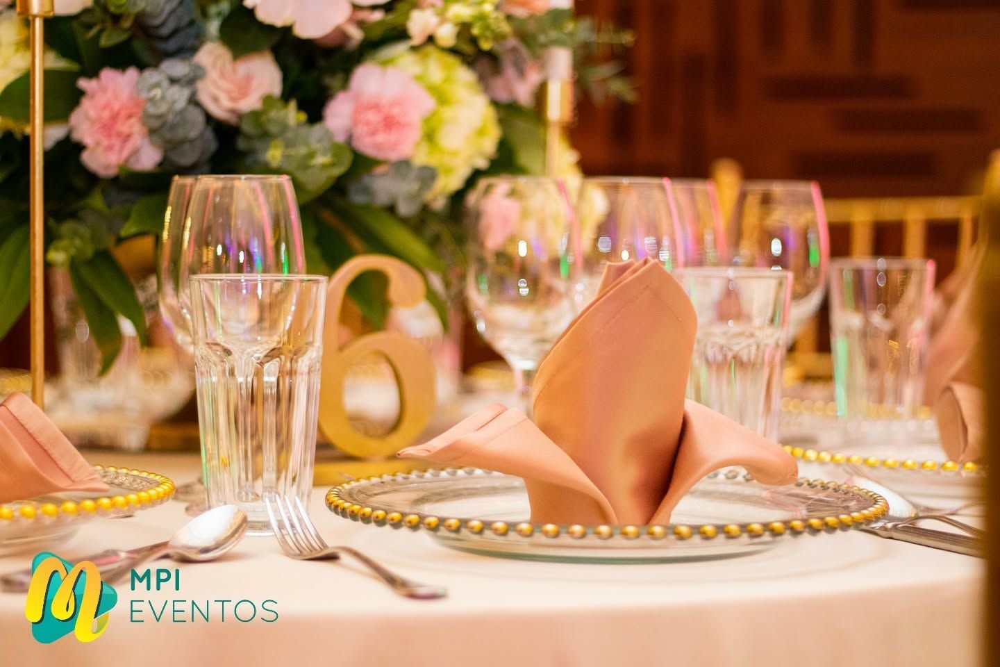 Elegante mesa de banquete con servilletas rosas, cristalería y un centro floral bajo una cálida iluminación