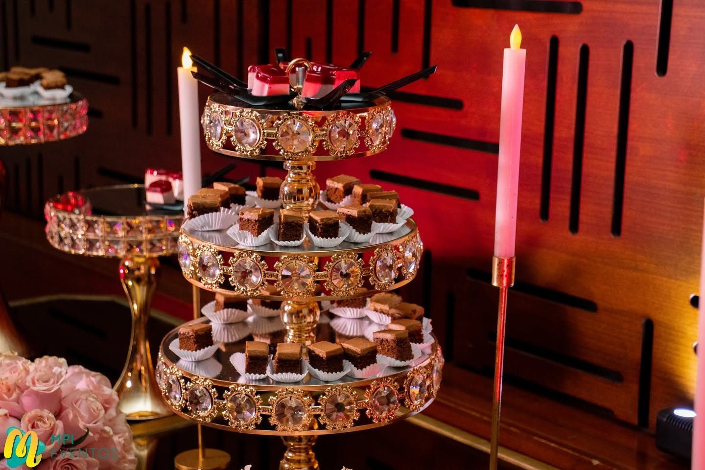 Soporte de postres de varios niveles con dulces y velas rosas sobre un fondo rojo cálido