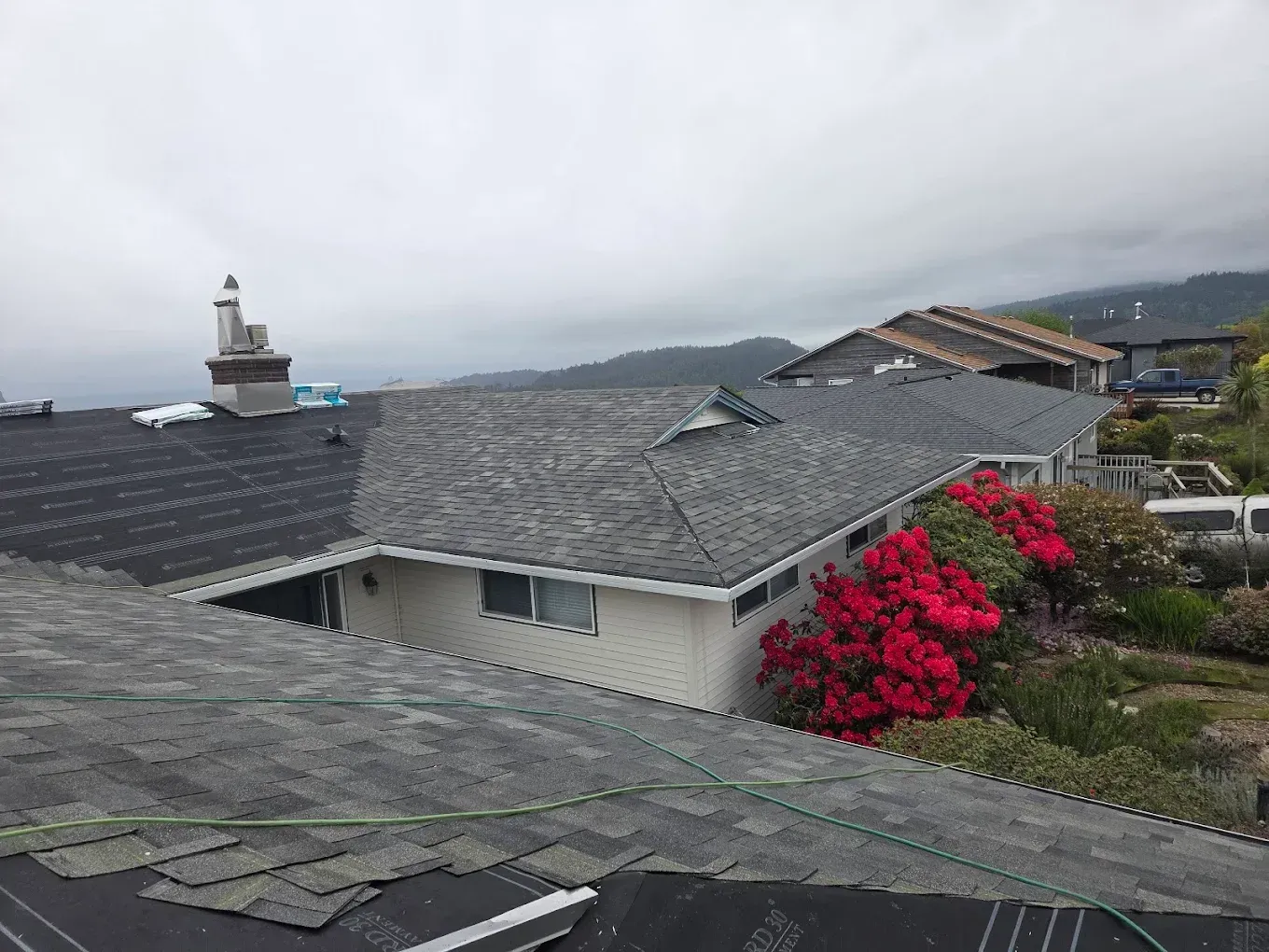 Houses with gray shingle roofs and red flowers under a cloudy sky.