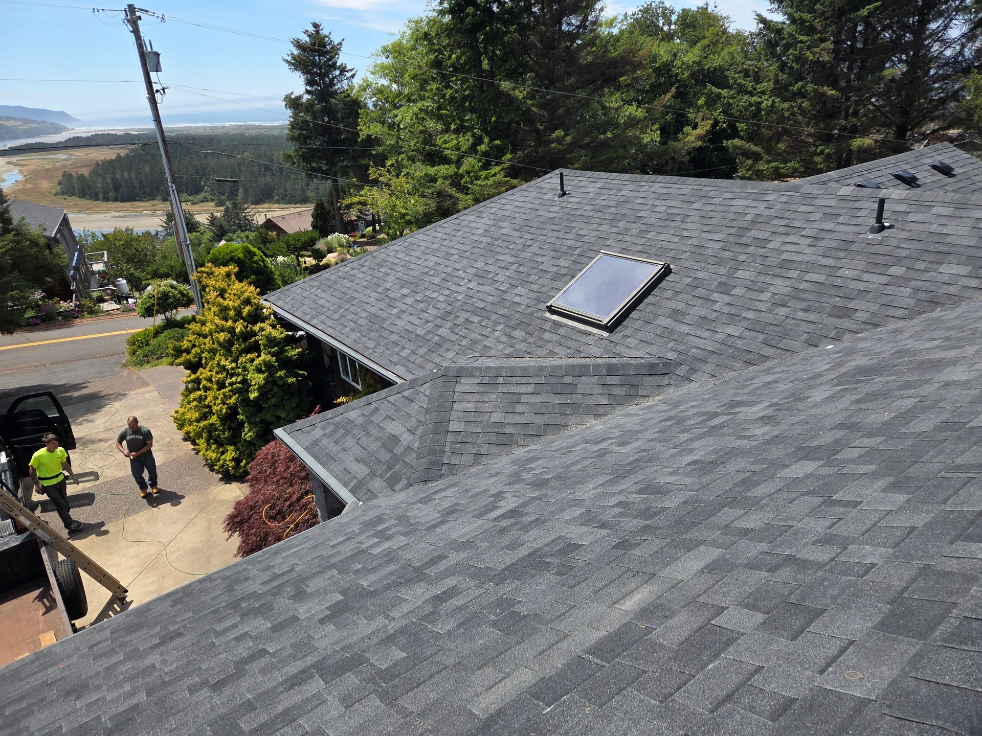 A dark-shingled roof with a solar panel and skylight. Two people and a car are on the ground below.