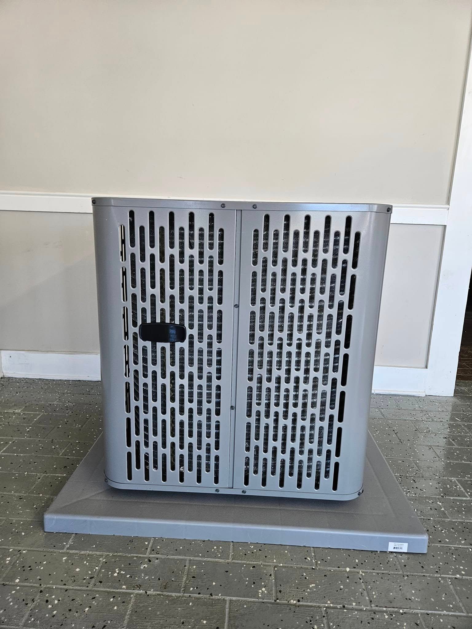 Gray metal vent cover on a mat against a beige wall indoors