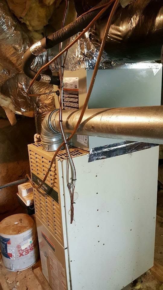 White furnace or HVAC unit in a cramped attic with exposed insulated ducts and wires.