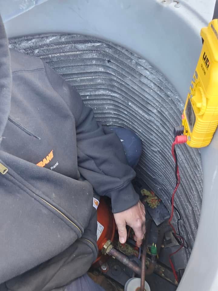Worker in a service shaft adjusting equipment beside coiled ducting and a yellow tool handle