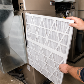 Person holding a white HVAC air filter beside a furnace unit.