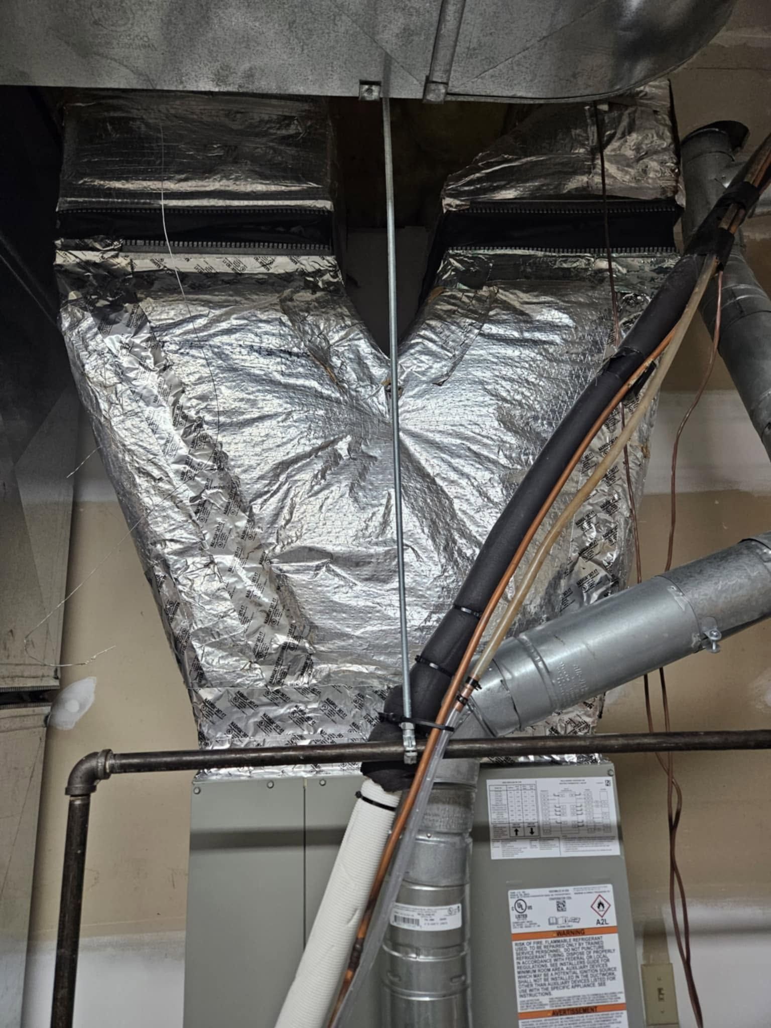 Foil-wrapped HVAC ductwork and pipes in a utility room ceiling area