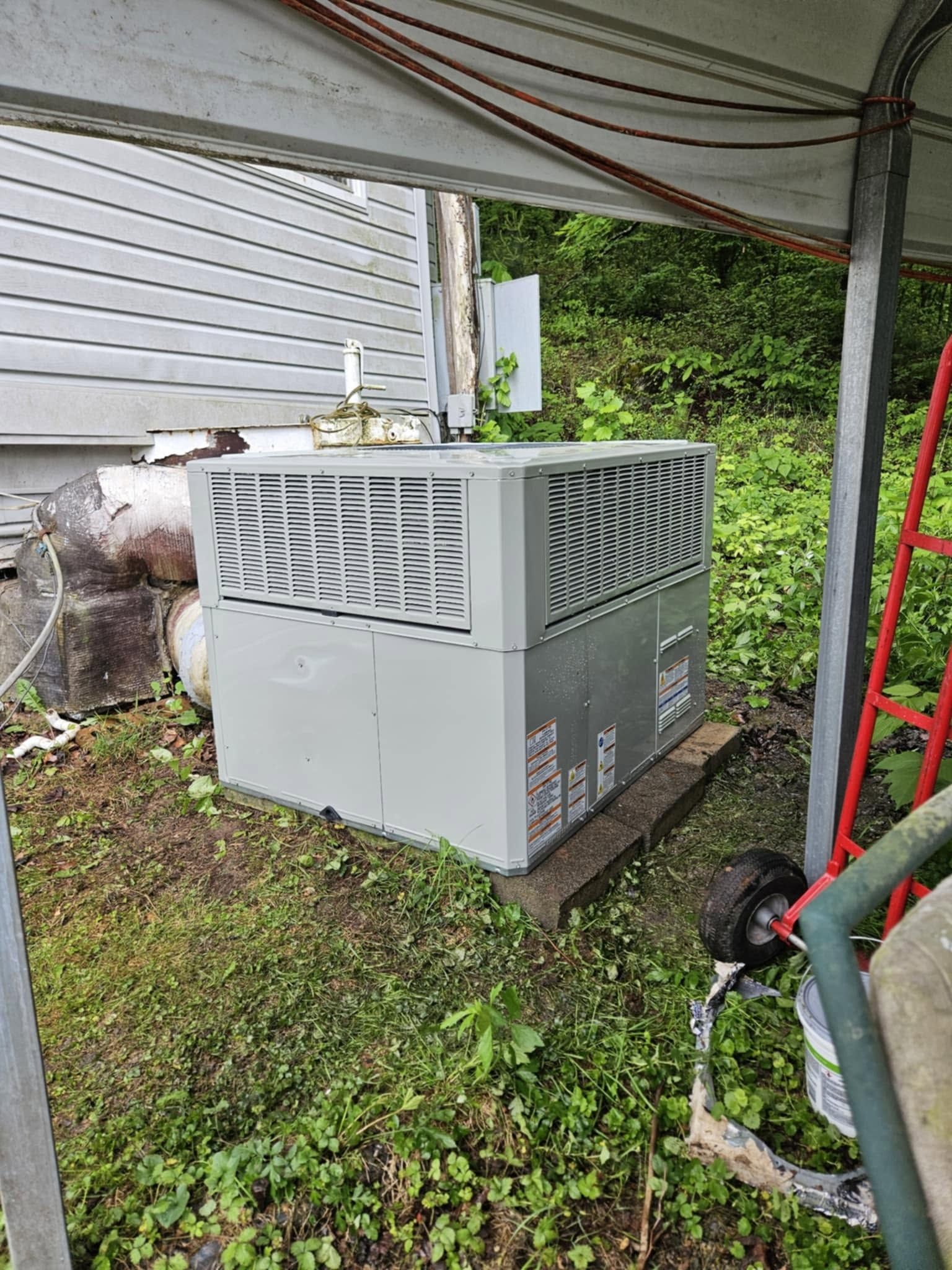 Large gray generator or HVAC unit under a covered patio beside a white house and grassy yard