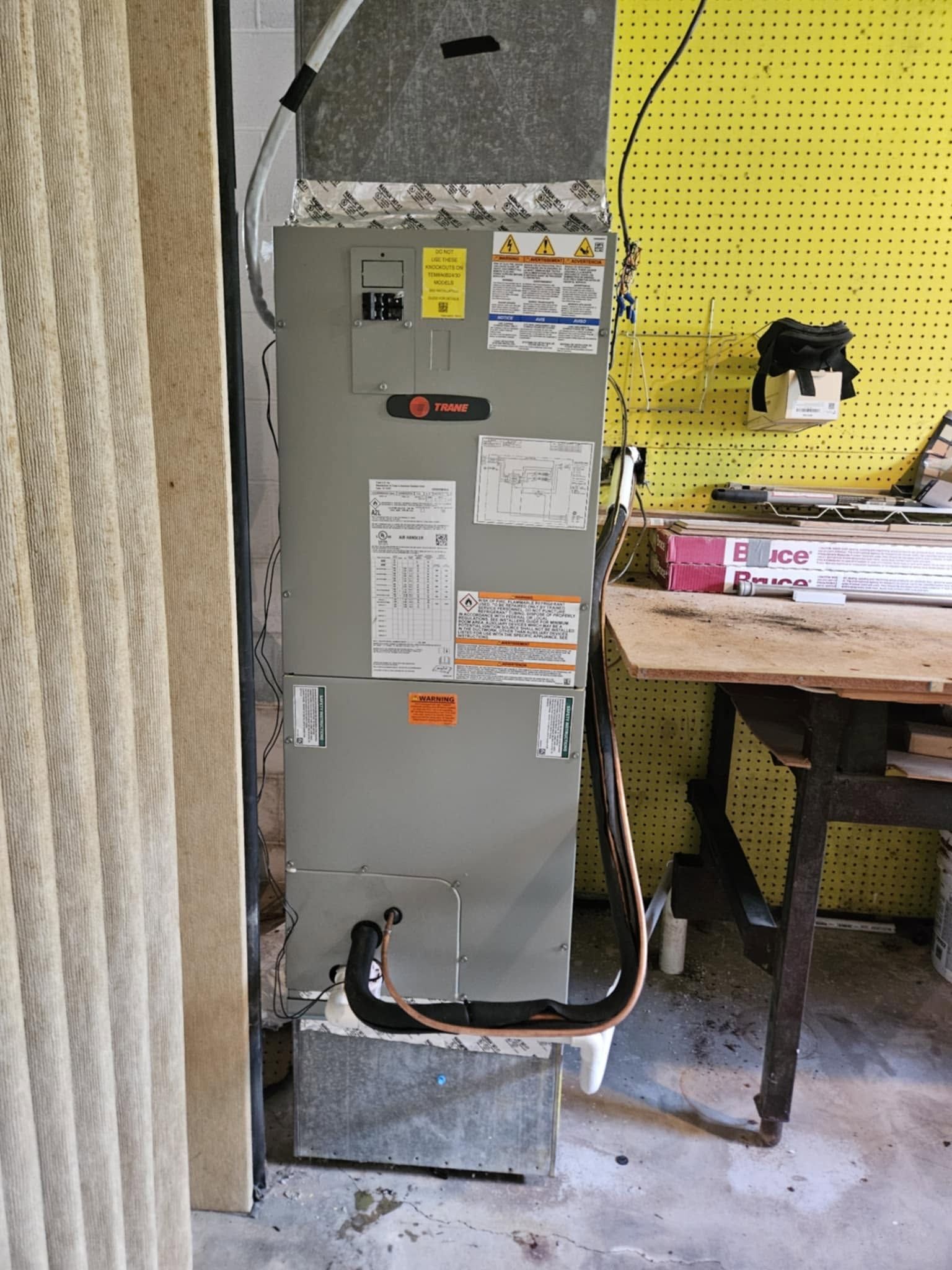 Gray furnace or HVAC unit in a utility closet beside a worktable and beige curtain.