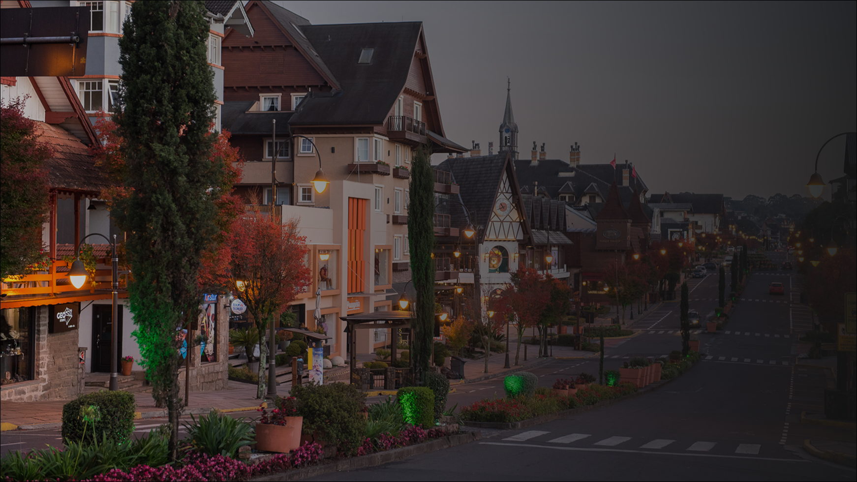 Uma rua numa cidade com arquitetura em estilo europeu, com estrutura de madeira aparente, ao entardecer, com iluminação aconchegante e árvores de outono.