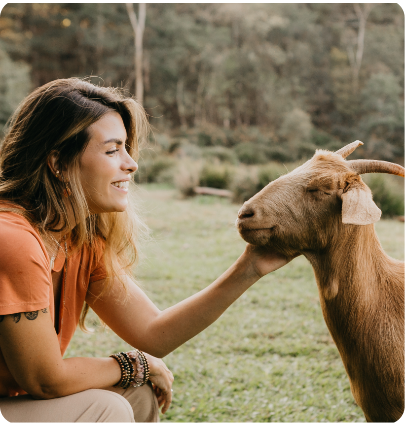 Mulher acariciando delicadamente uma cabra marrom em um campo gramado.