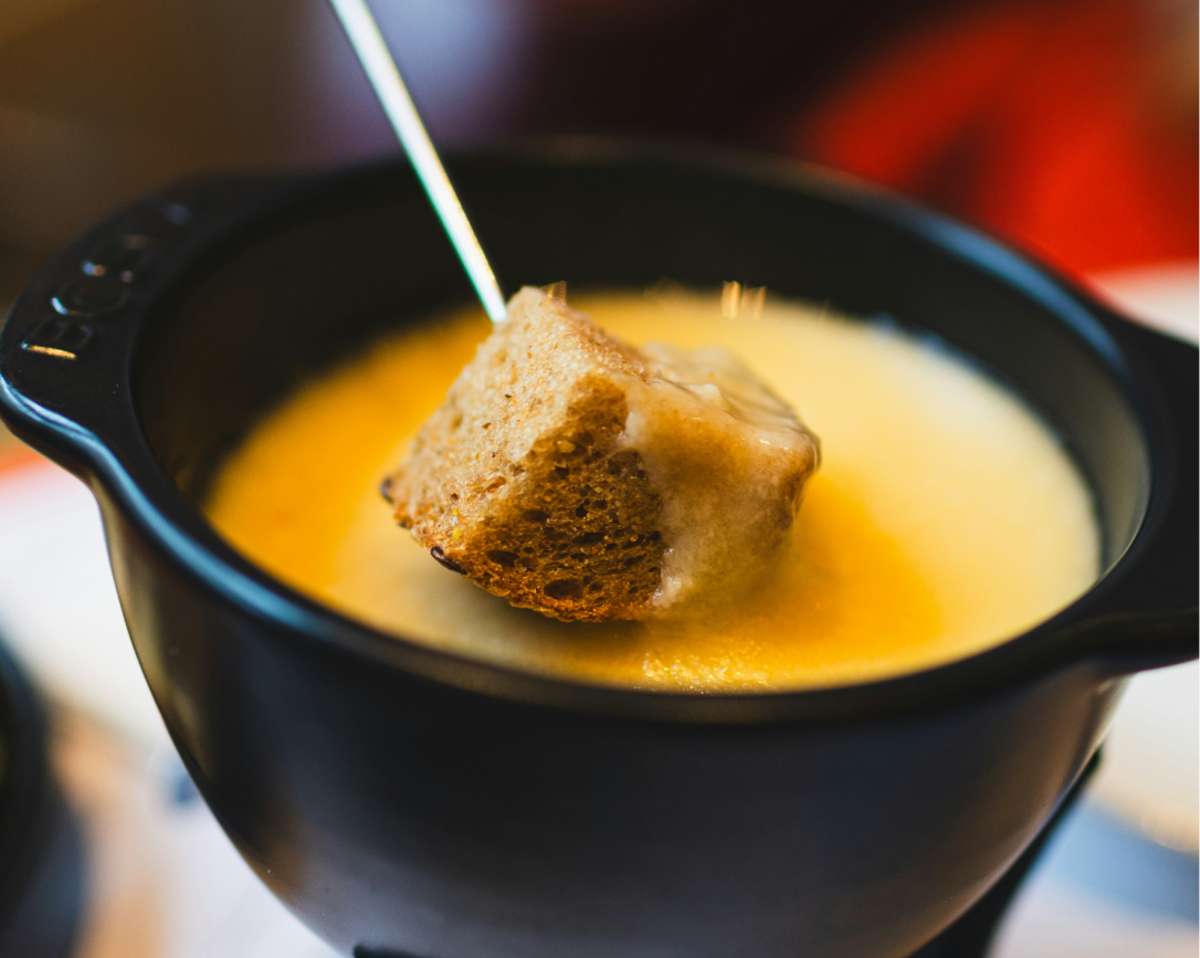 Panela de fondue com queijo derretido e um cubo de pão no espeto.