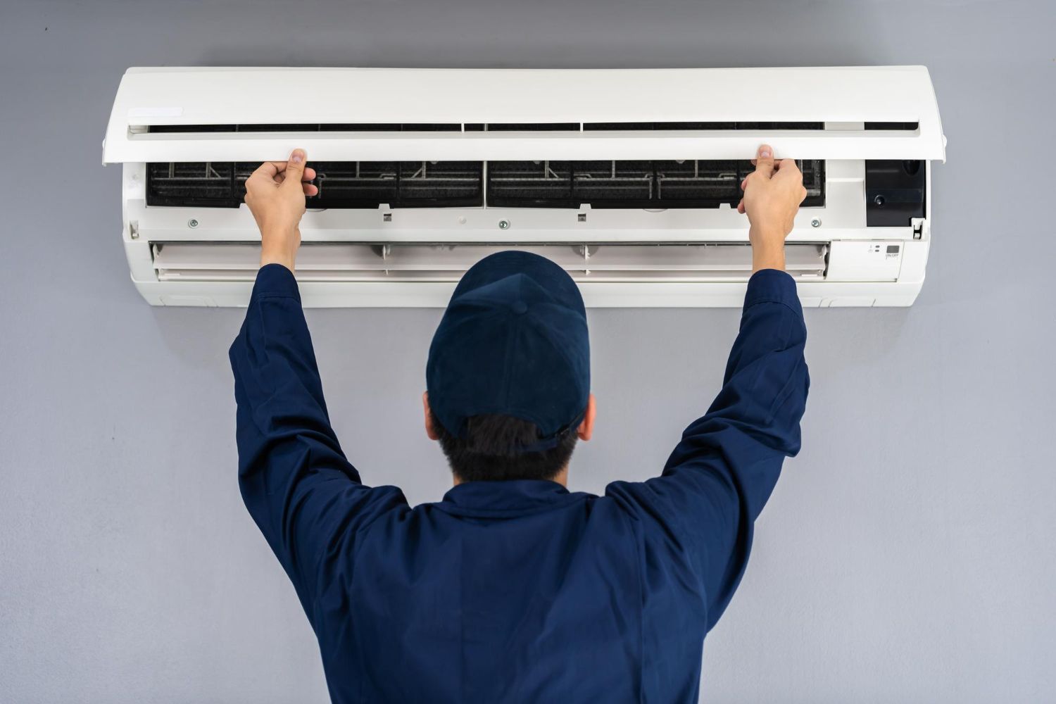 Technician adjusting a wall-mounted air conditioner with both hands