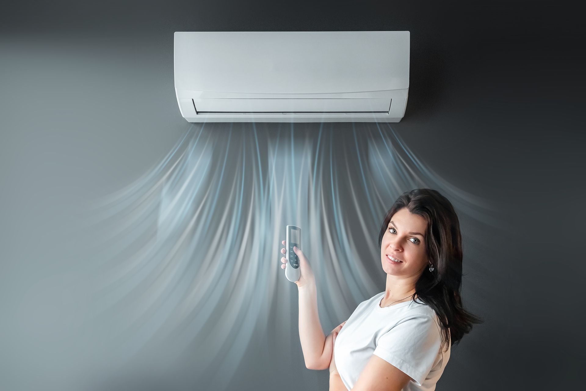 A person smiling while using a remote to control a wall-mounted air conditioner blowing cool air into a room.