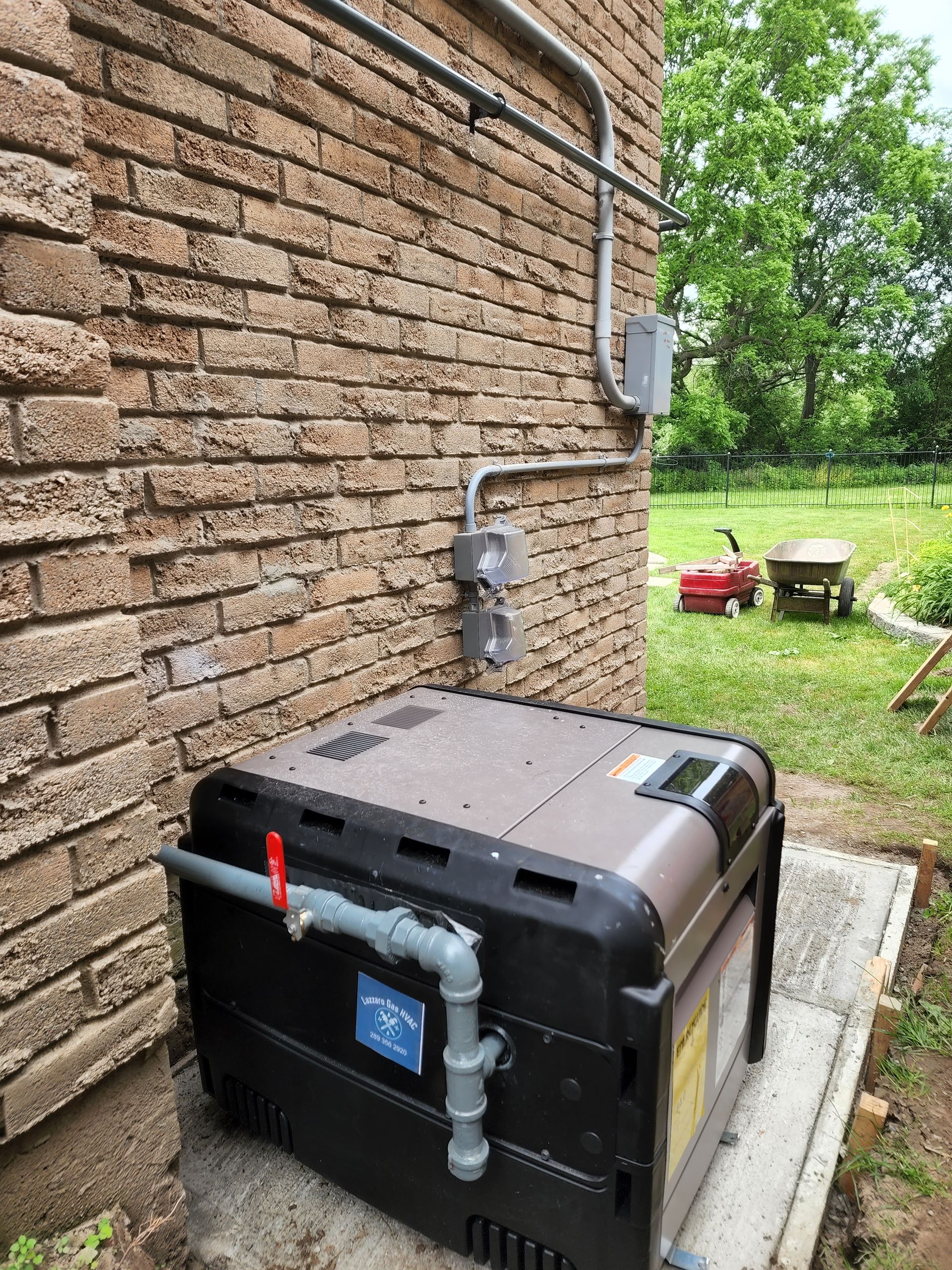 Outdoor HVAC unit beside a brick house, with pipes and wiring mounted on the wall.