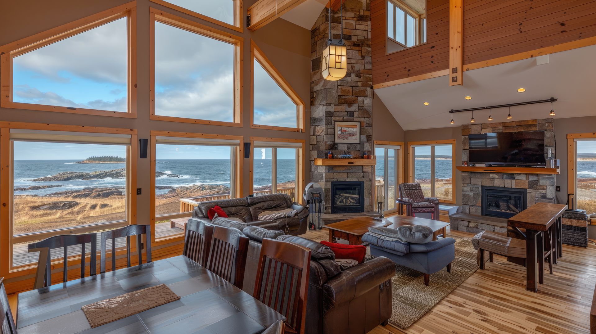 A spacious, rustic living room with floor-to-ceiling windows overlooking a rocky coastline and the ocean.