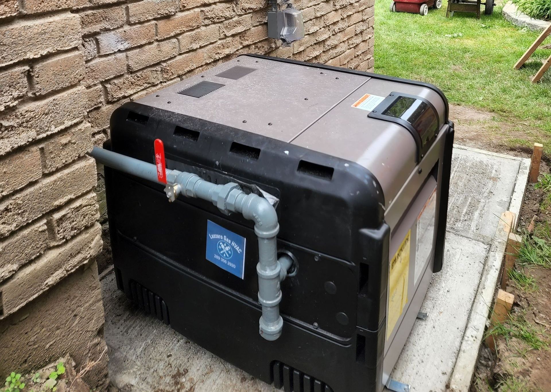 A black box with a valve attached to it is sitting on the ground next to a brick wall.