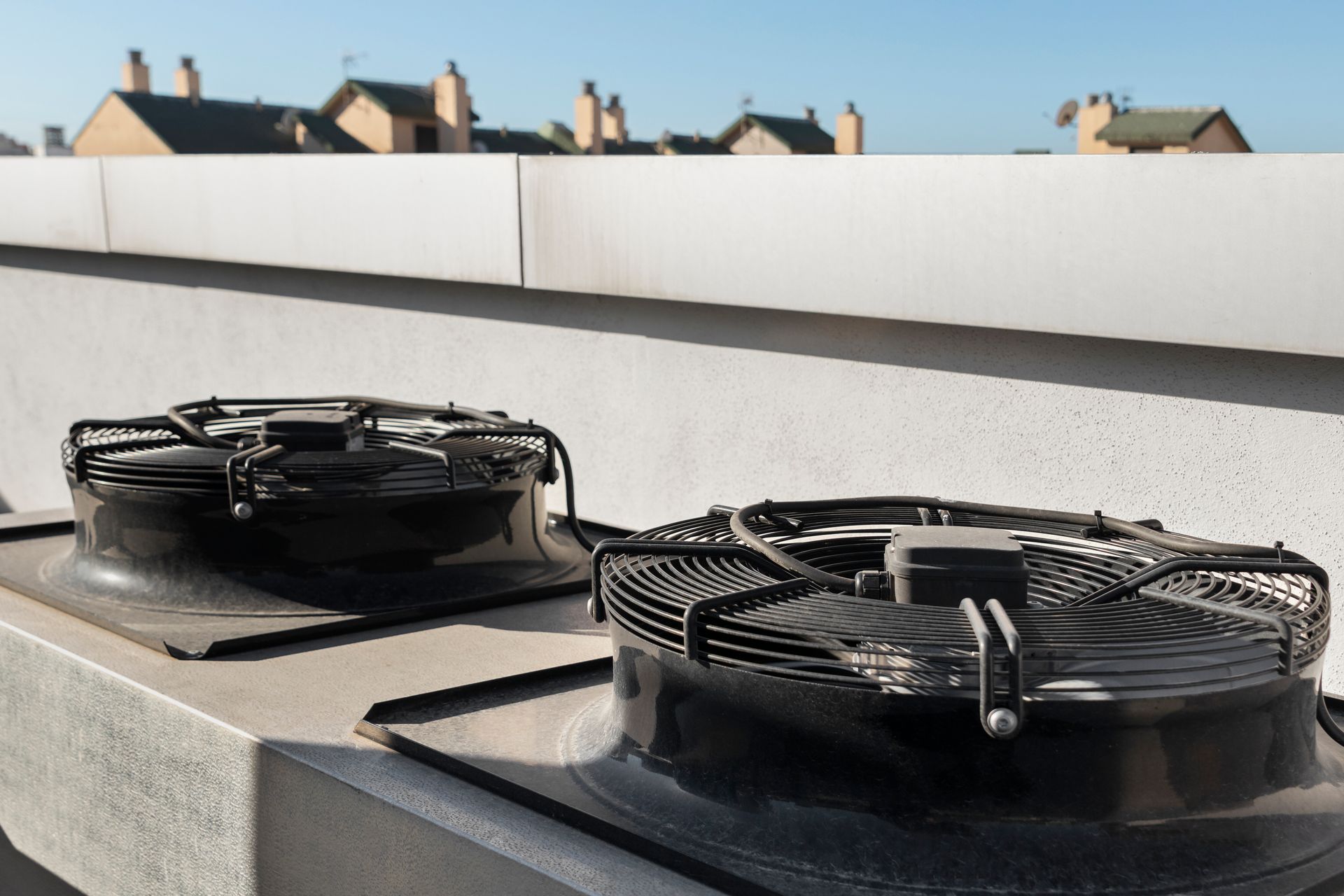 Two rooftop ventilation fans on a flat roof with a white parapet and buildings in the background