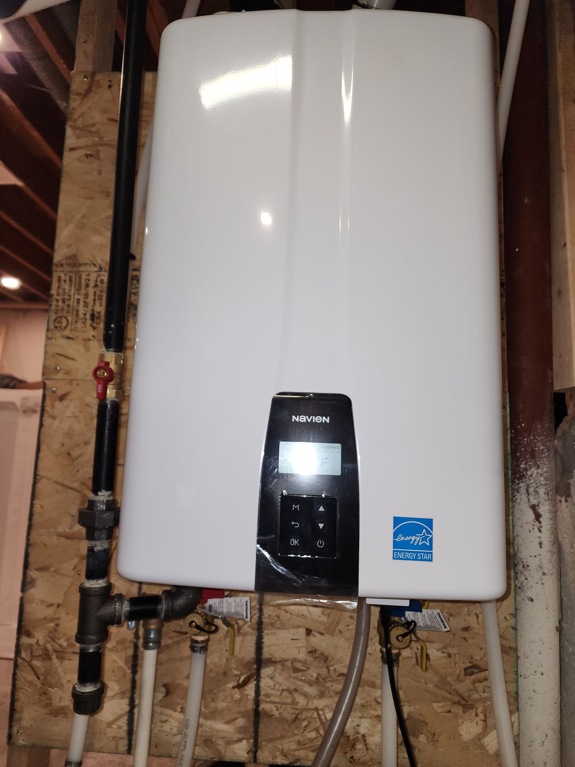 White wall-mounted water heater with black control panel in a utility space with exposed wall framing.