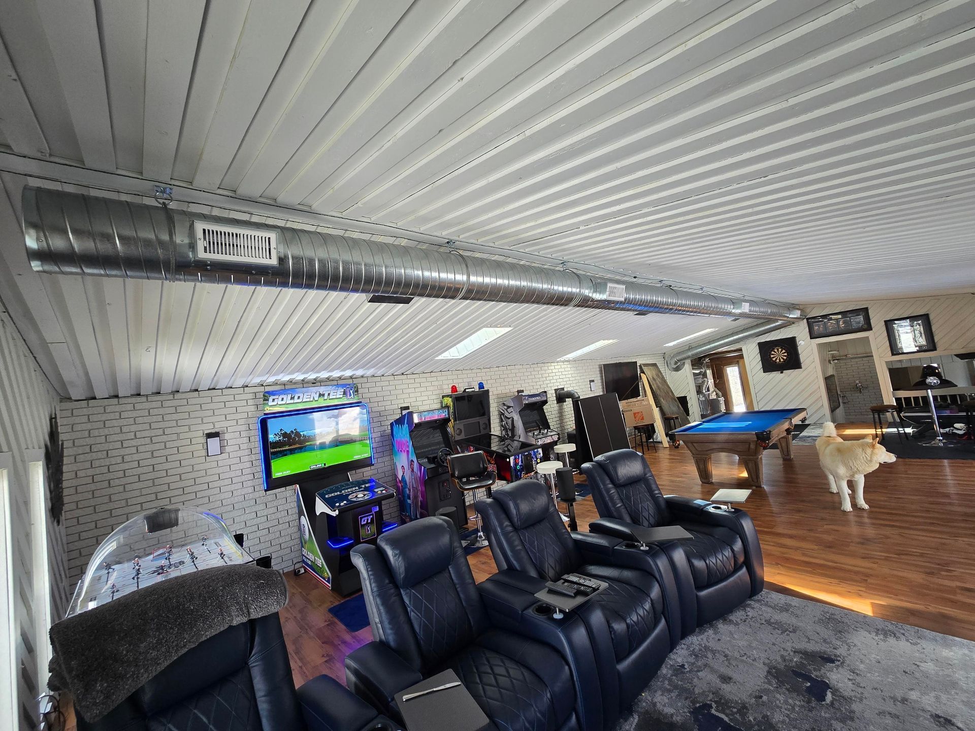 Lounge with black recliners, a TV, arcade machines, and wood flooring under a silver ceiling
