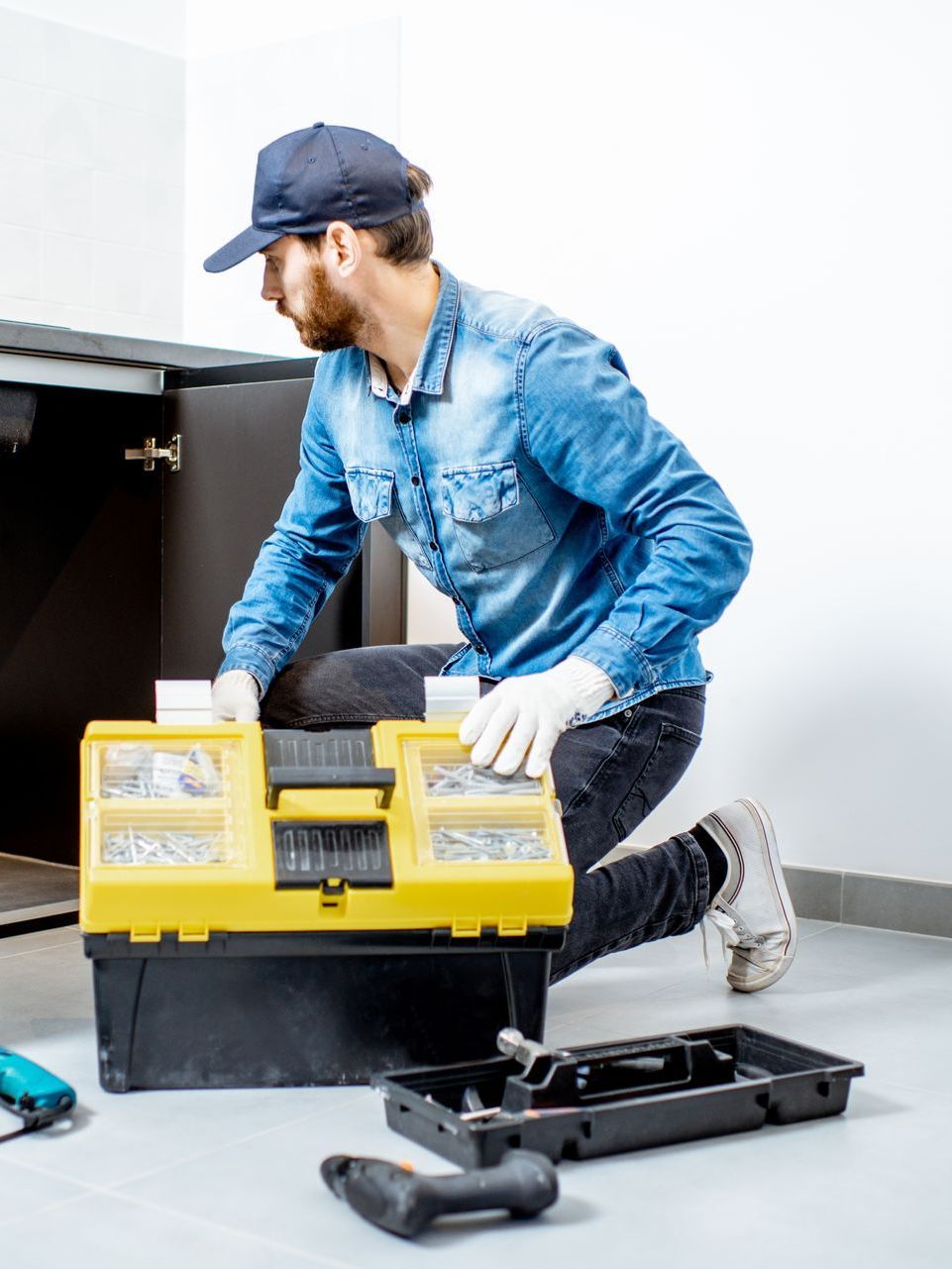 A man is kneeling down next to a toolbox in a kitchen.
