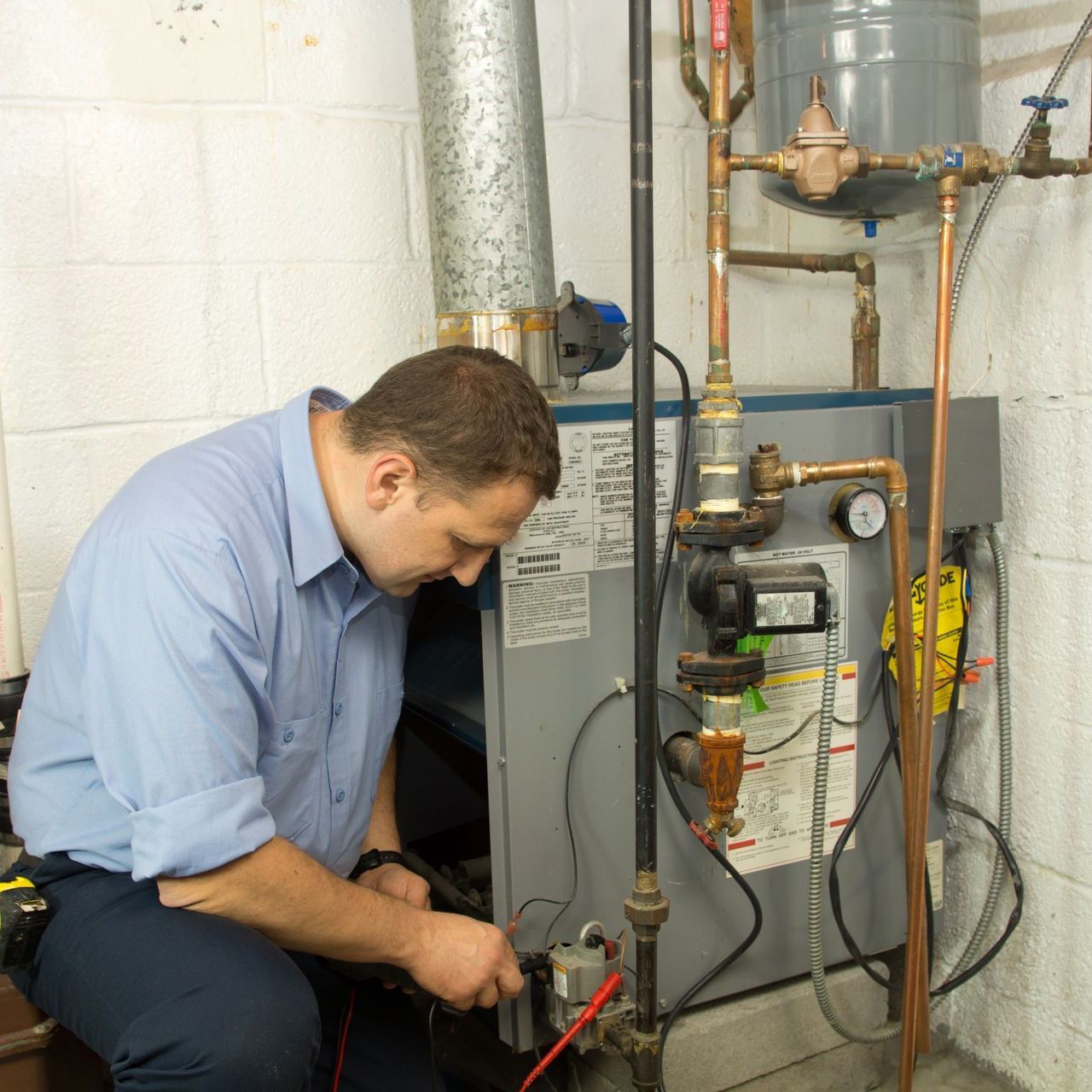 A man is working on a water heater in a basement