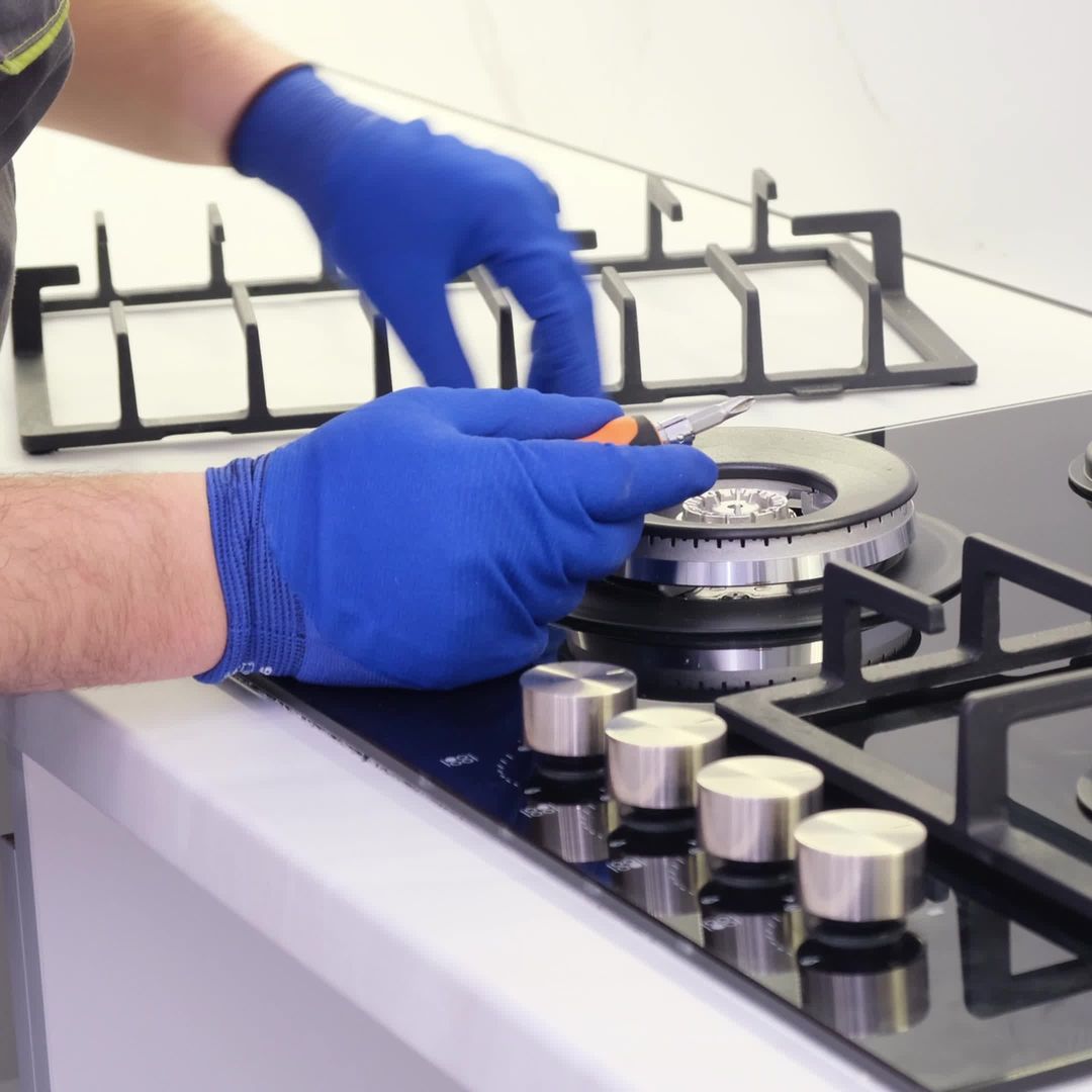 A person wearing blue gloves is working on a stove top