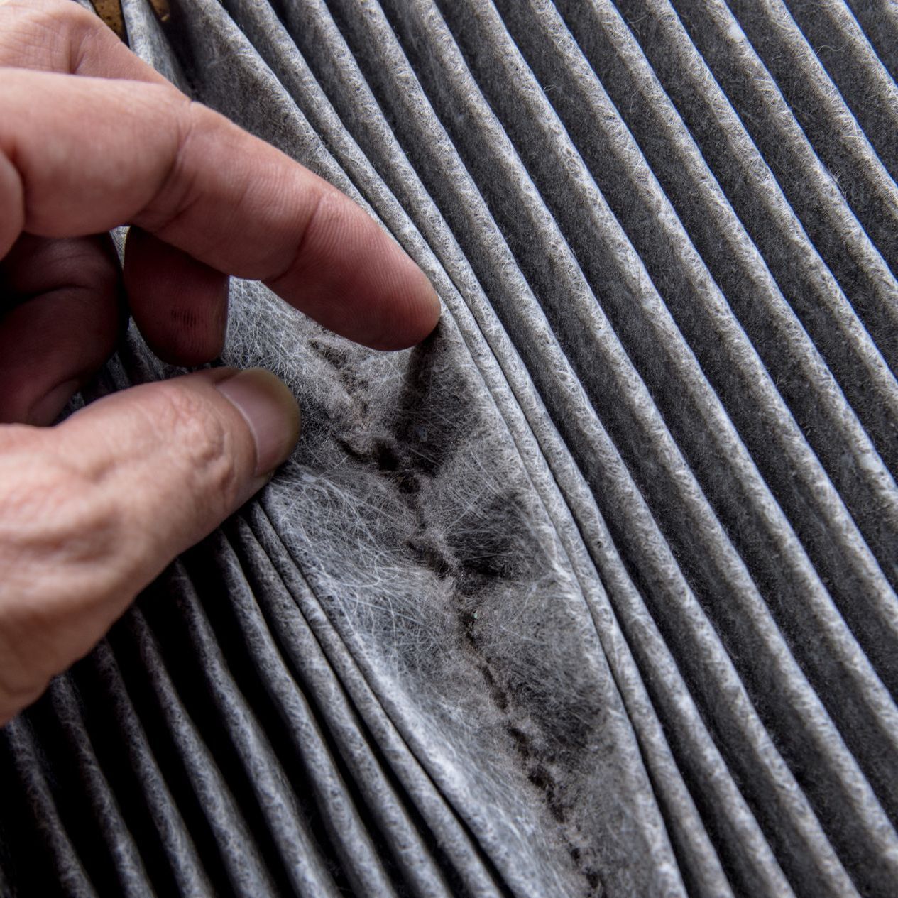 A person is touching a dirty air filter with their finger