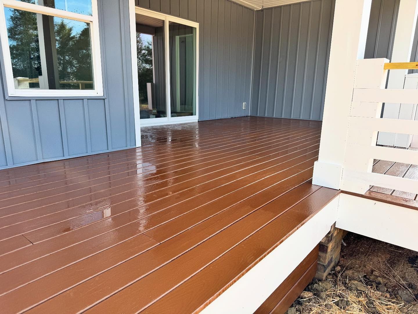 A newly painted brown deck with reflections, attached to a blue-gray house. White trim and a window are also visible.