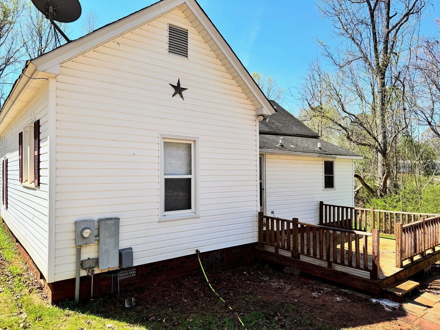 White house with a small wooden deck. A star is mounted on the gable. The setting is outdoors on a sunny day.