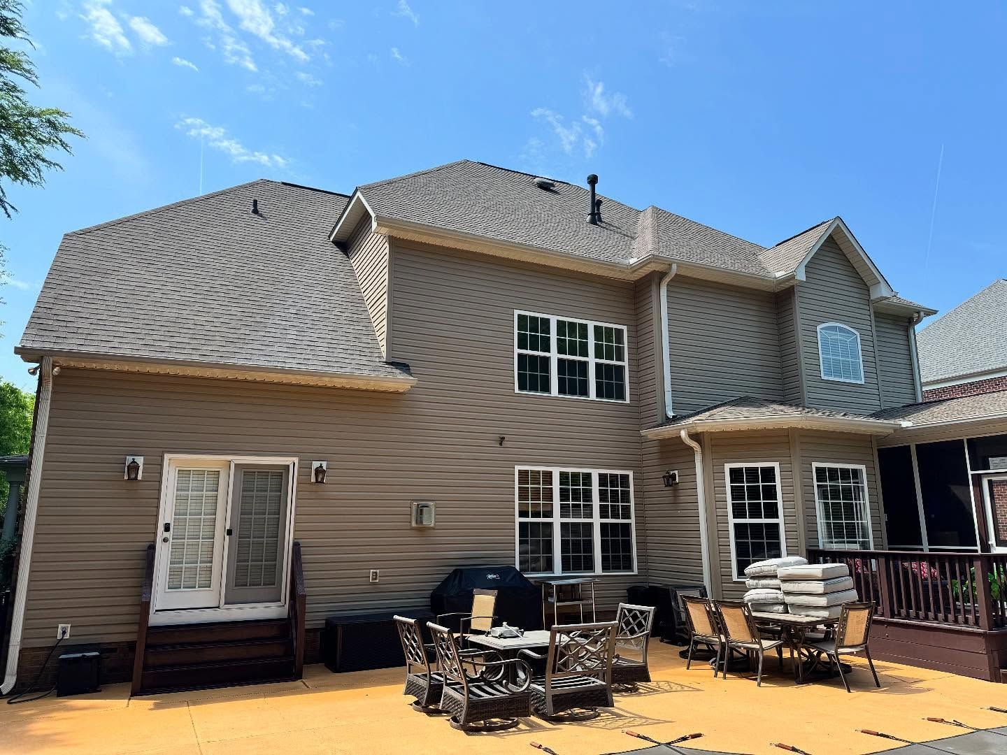 Back view of a two-story house with brown siding, a brown roof, and a patio area with outdoor furniture.