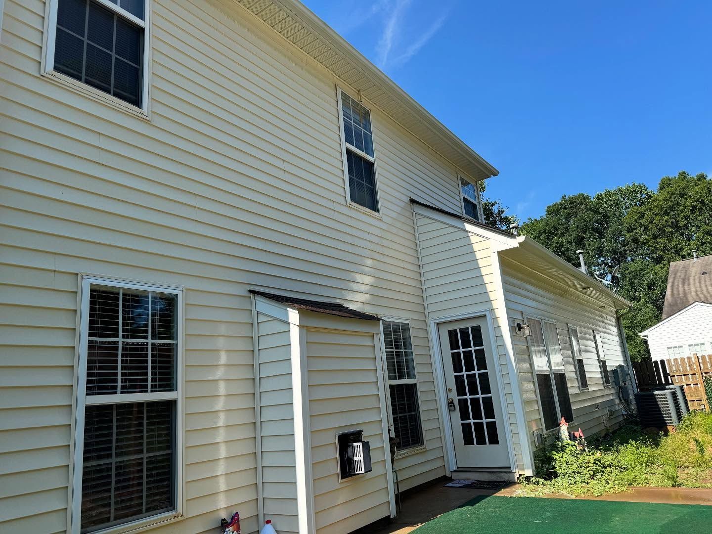 Exterior of a two-story house with light yellow siding, multiple windows, and a 