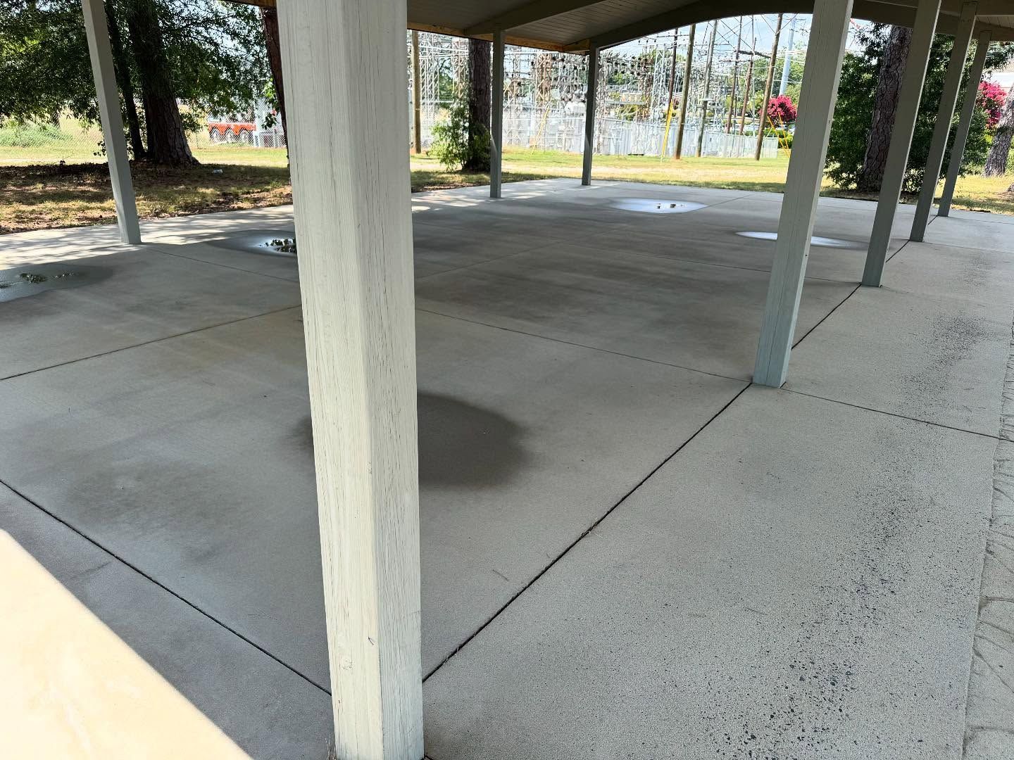 Concrete shelter with several support columns and a view of trees and water in the background.