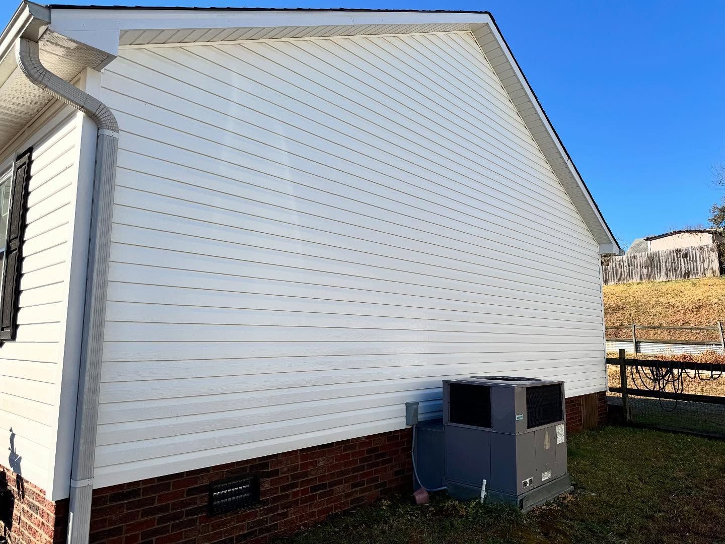 Side of a white house with vinyl siding, brick base, and an HVAC unit on the lawn.
