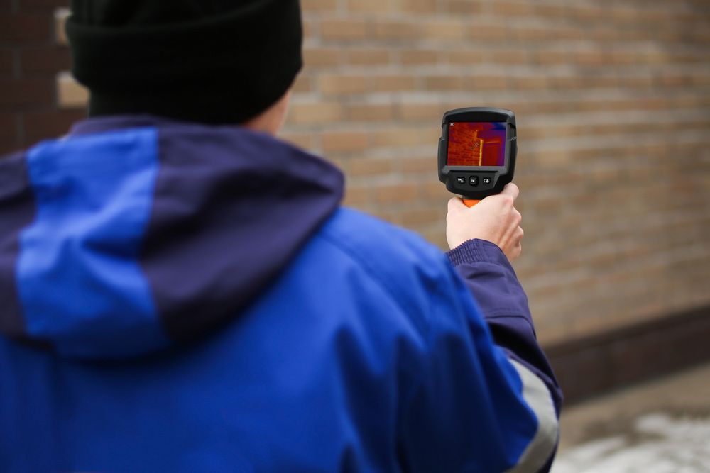 A Man Is Holding A Thermal Camera In Front Of A Brick Wall — Tweed Heads Leak Detection in Casuarina, NSW