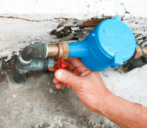 A Person Is Holding A Red Valve Next To A Water Meter — Tweed Heads Leak Detection in Casuarina, NSW