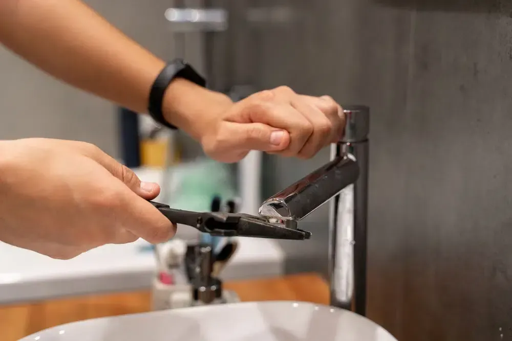 A Person Is Fixing A Bathroom Sink Faucet With A Wrench — Tweed Heads Leak Detection in Ballina, NSW