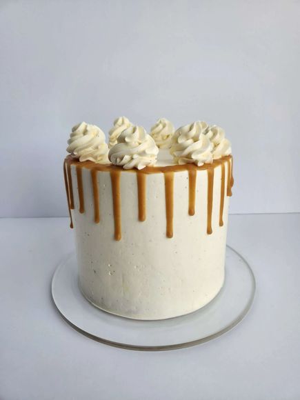 White frosted cake with caramel drips and whipped cream swirls on a white plate