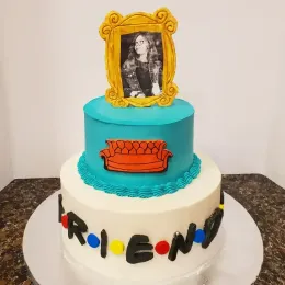 Tiered Friends-themed cake with blue, white, and black decorations and a framed black-and-white portrait topper