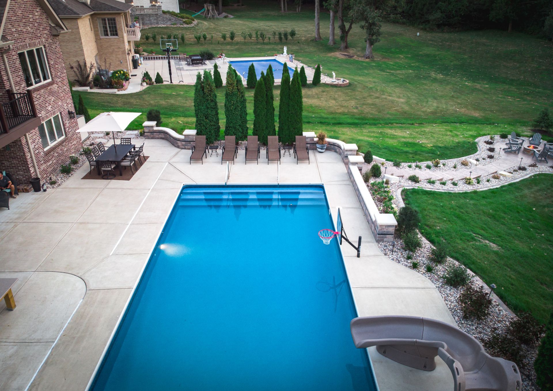 Backyard pool with blue water, patio chairs, and a landscaped lawn beside a brick house