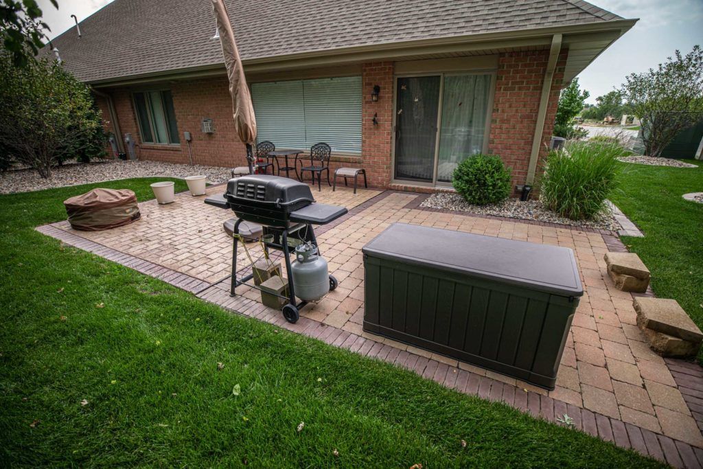 A brick patio with a grill and umbrella in front of a brick house.
