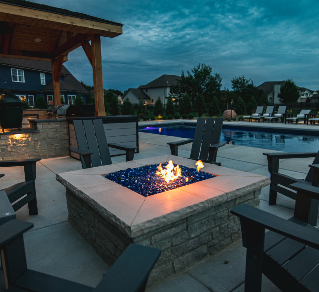 A fire pit with chairs around it and a pool in the background