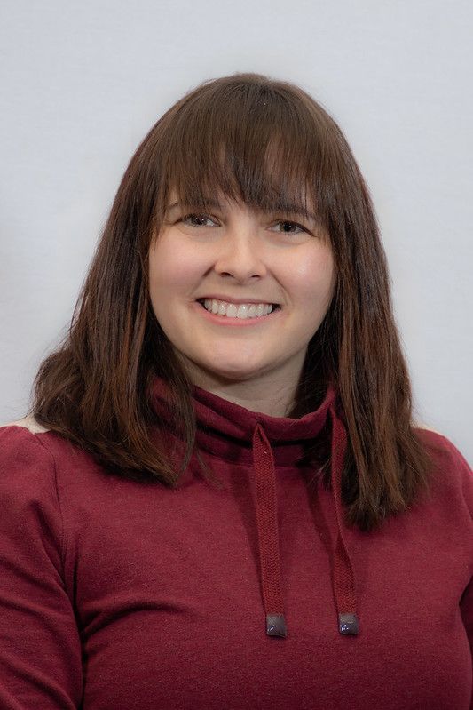 Woman with brown hair and bangs smiles, wearing a burgundy turtleneck in front of a white background.