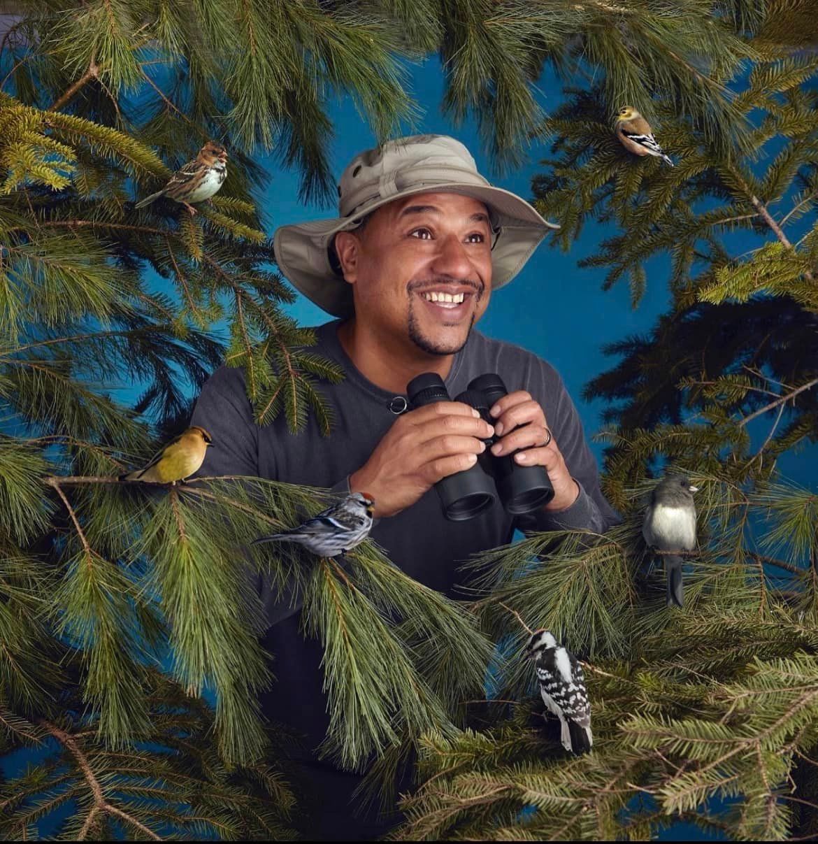 Man holding binoculars looking through pine branches surrounded by birds