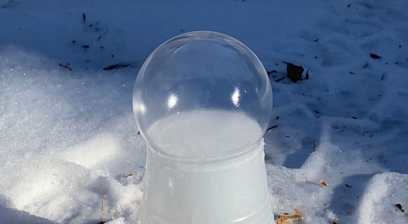 Clear bubble filled with vapor, sitting atop a white container in snowy outdoors.