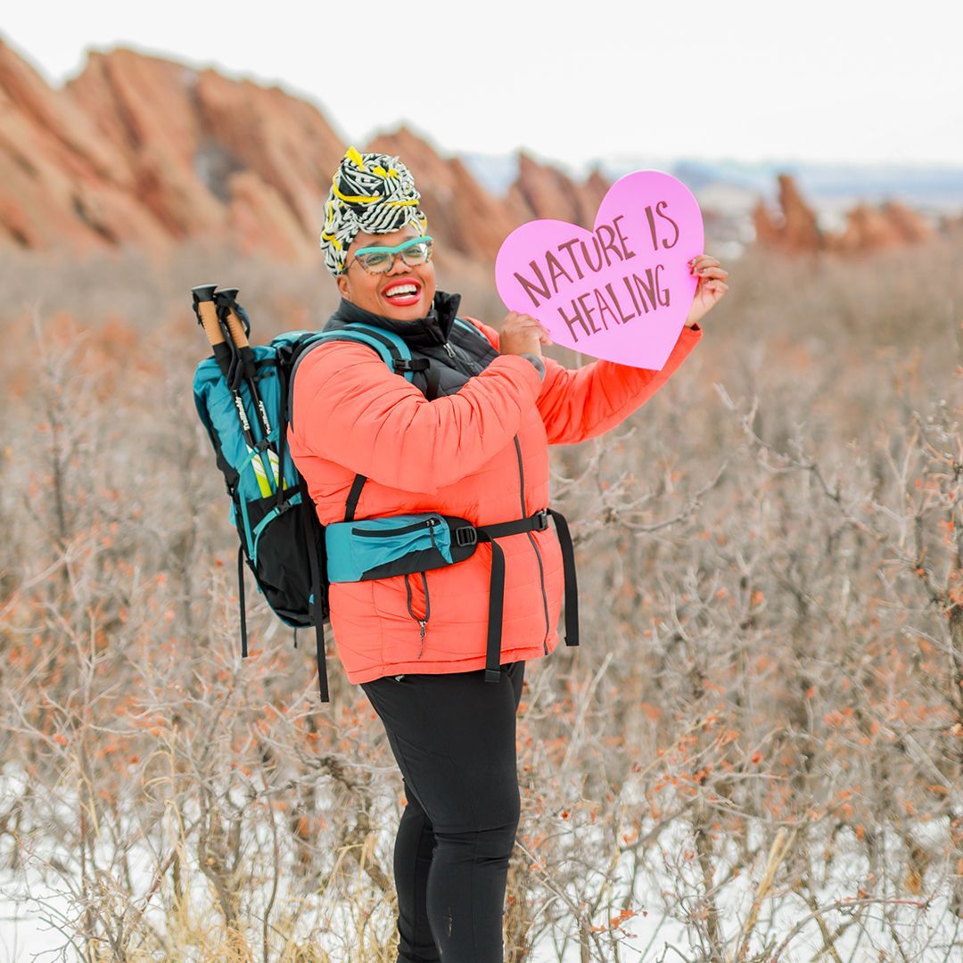 Woman outside wearing a backpack and holding a heart-shaped sign that reads 