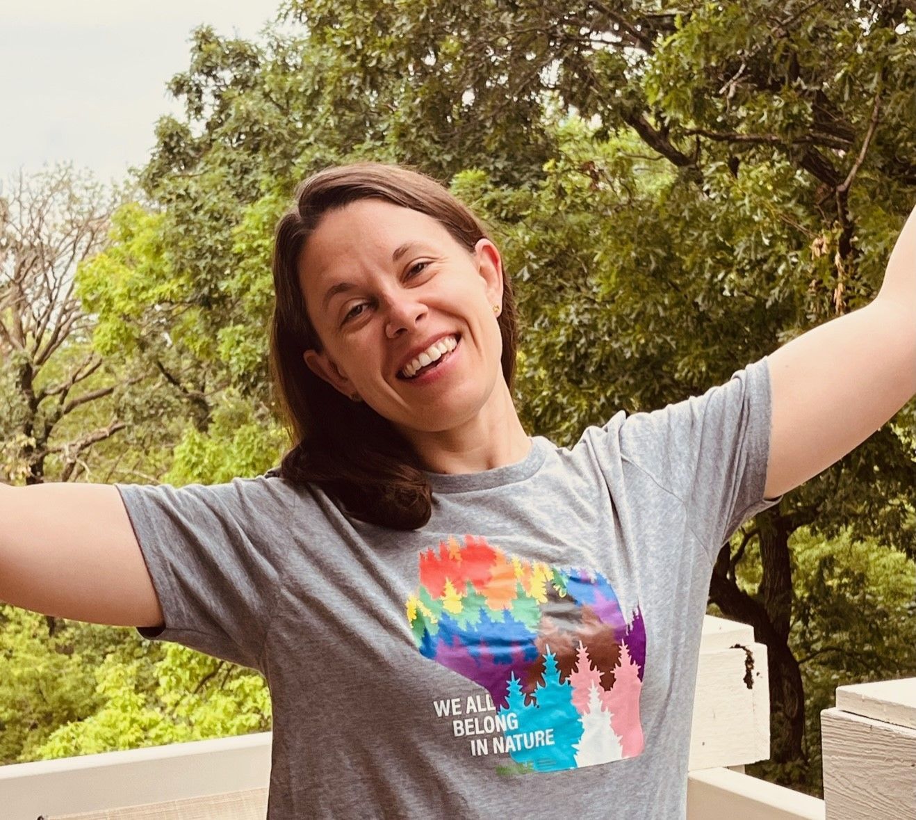 Woman outdoors wearing a tshirt with an image of wisconsin covered in a rainbow of trees